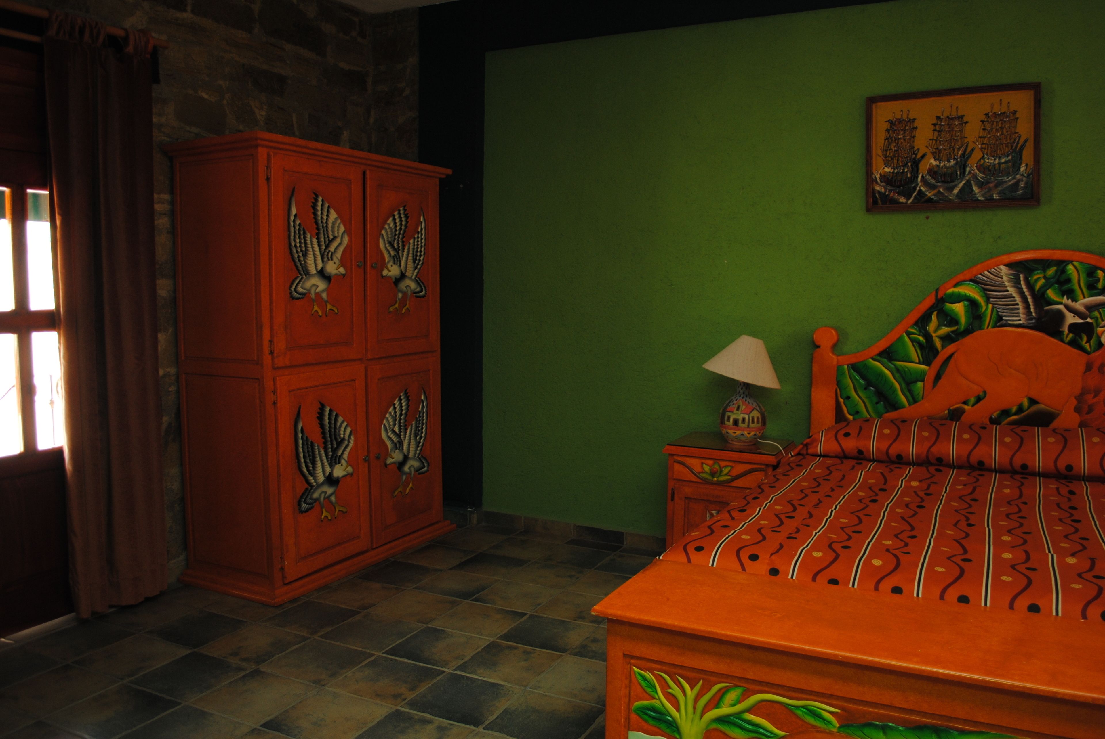 A bedroom with a bed, a nightstand, a cabinet with eagle designs, a green wall, and a framed picture.