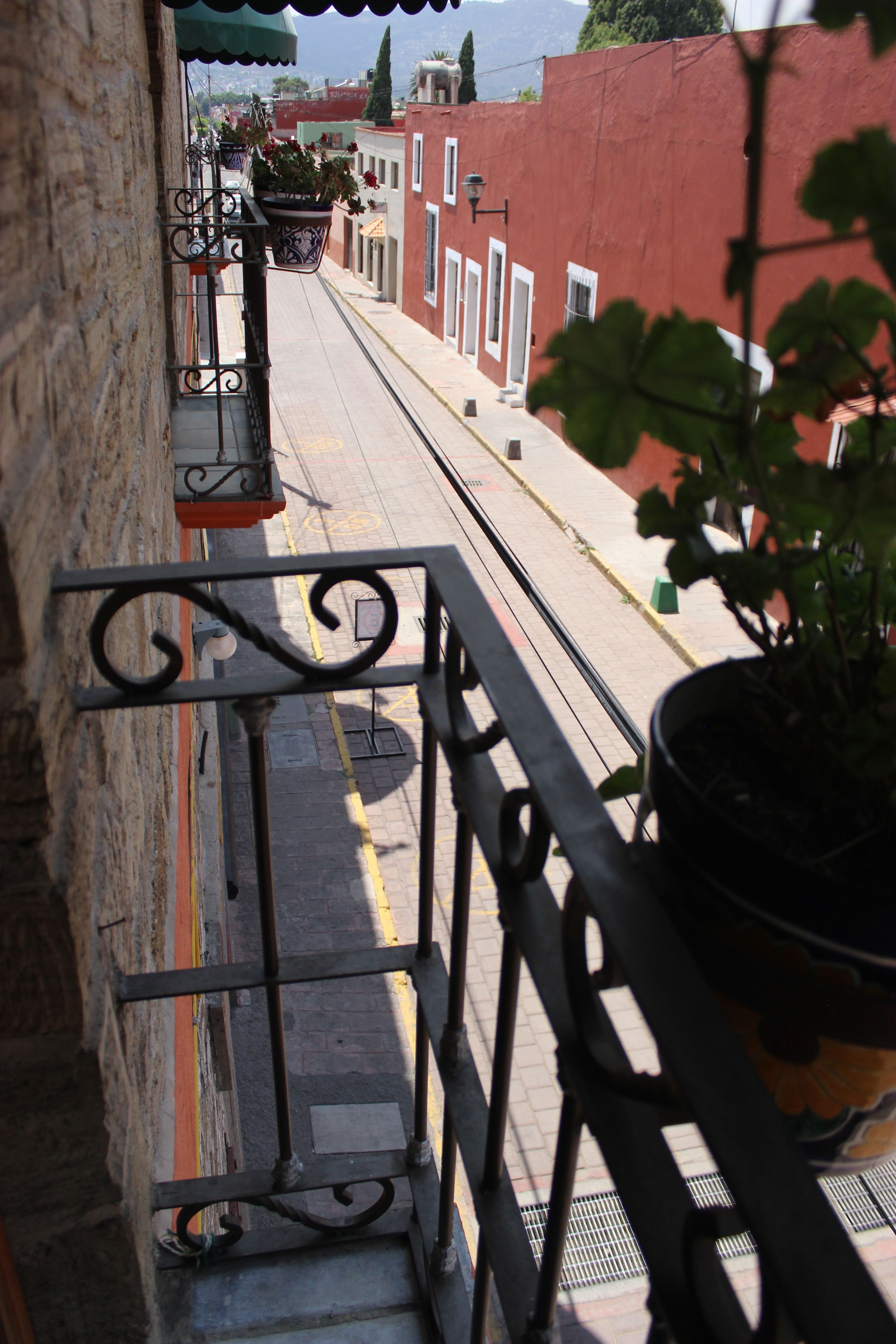 Una calle estrecha flanqueada por edificios, una barandilla metálica y macetas con plantas.