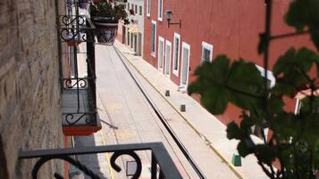 Una calle estrecha flanqueada por edificios, una barandilla metálica y macetas con plantas.