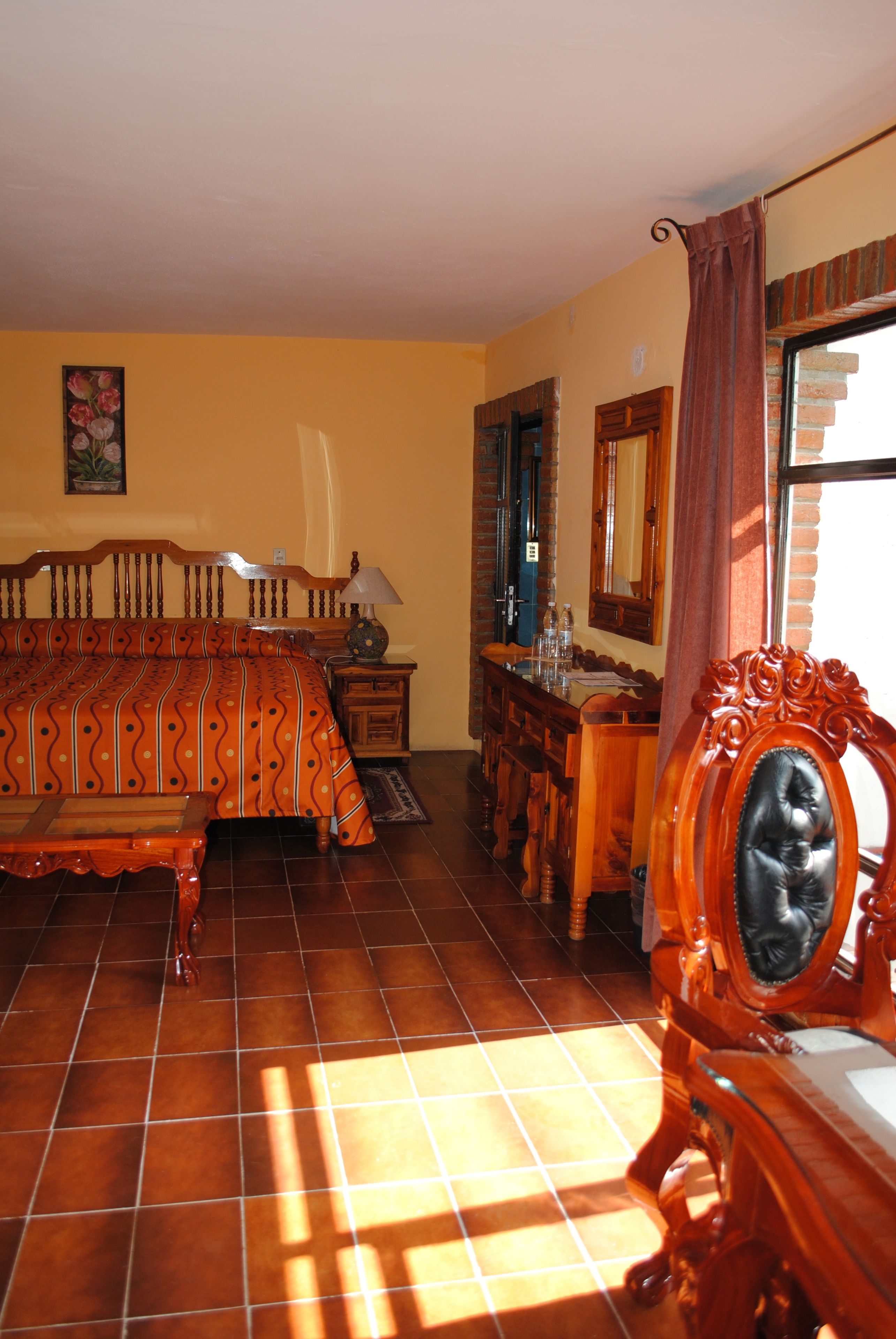 Een kamer met een bed, een houten dressoir, een spiegel en een raam met gordijnen.