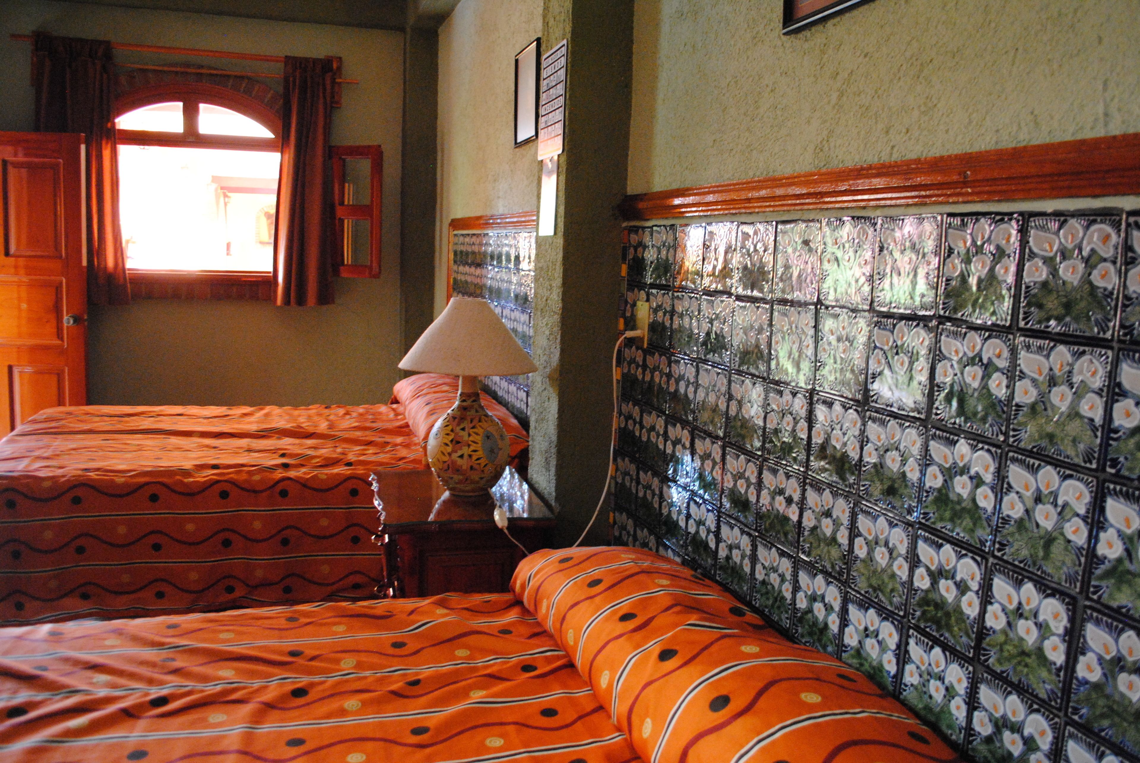 A hotel room with two beds, a lamp, and a tiled wall.