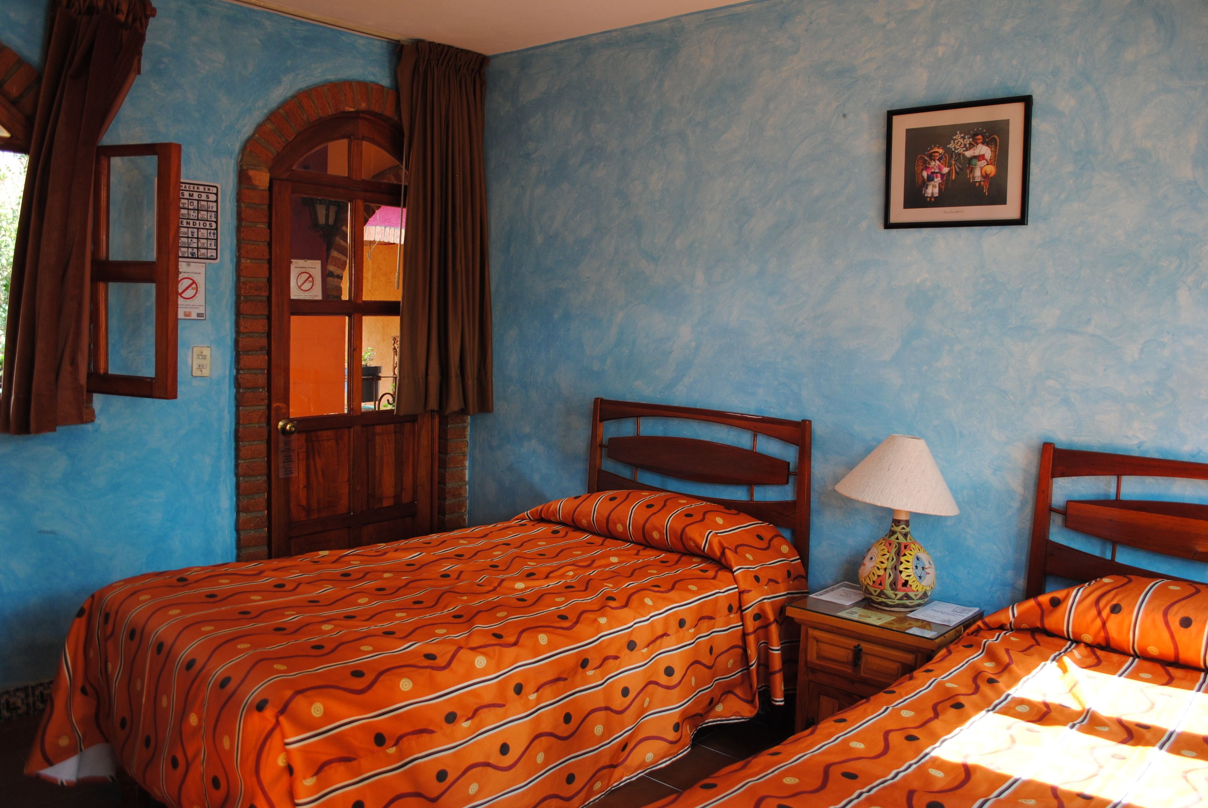 A room with a bed, a nightstand, a lamp, a framed picture, and a door with a window.
