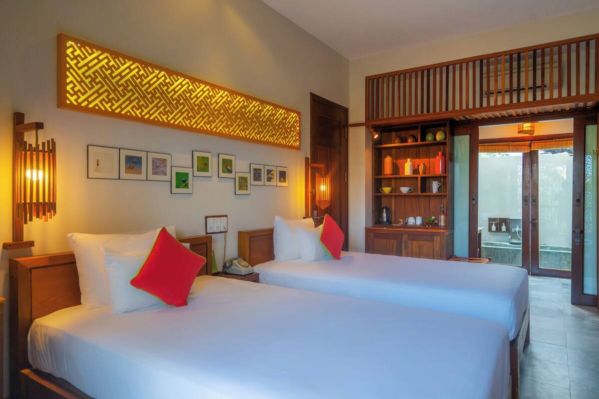 A hotel room with two beds, a wooden headboard, a decorative wall panel, and a view of the outside.