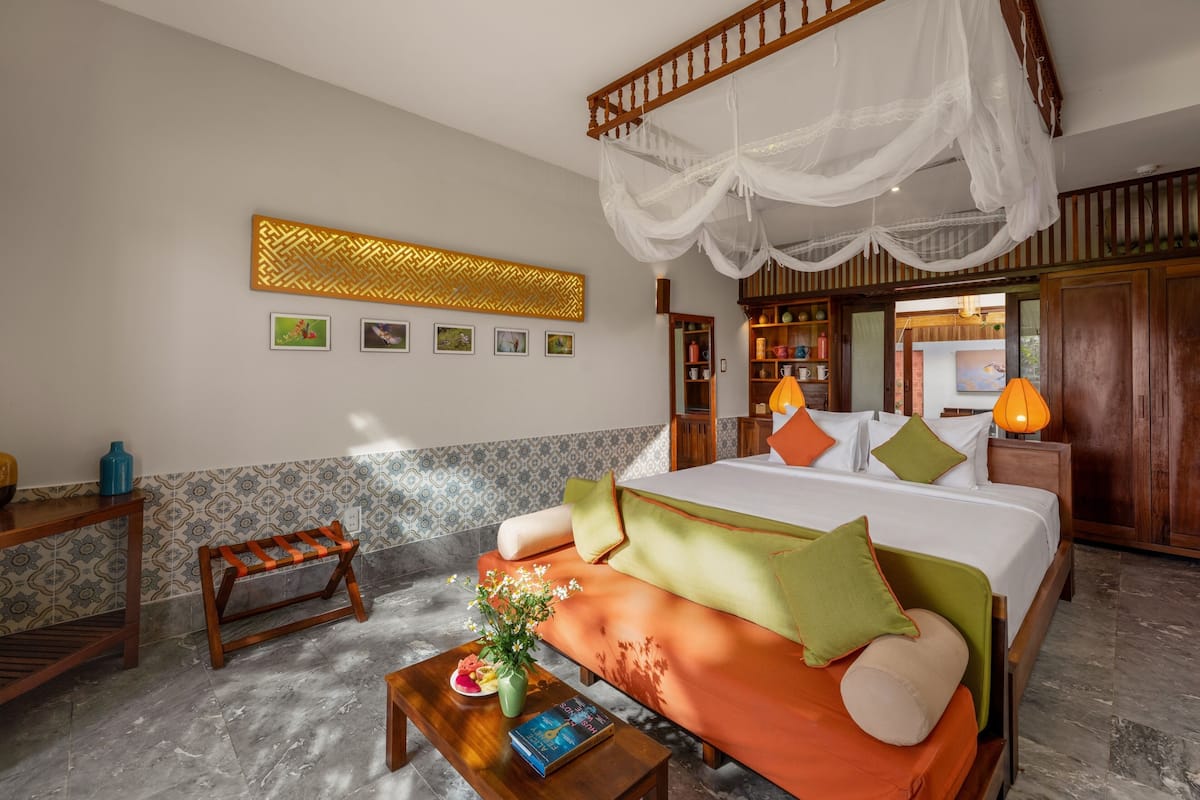 A bedroom with a bed, a nightstand, a bedside table, a chair, a decorative wall piece, a bookshelf, and a window.