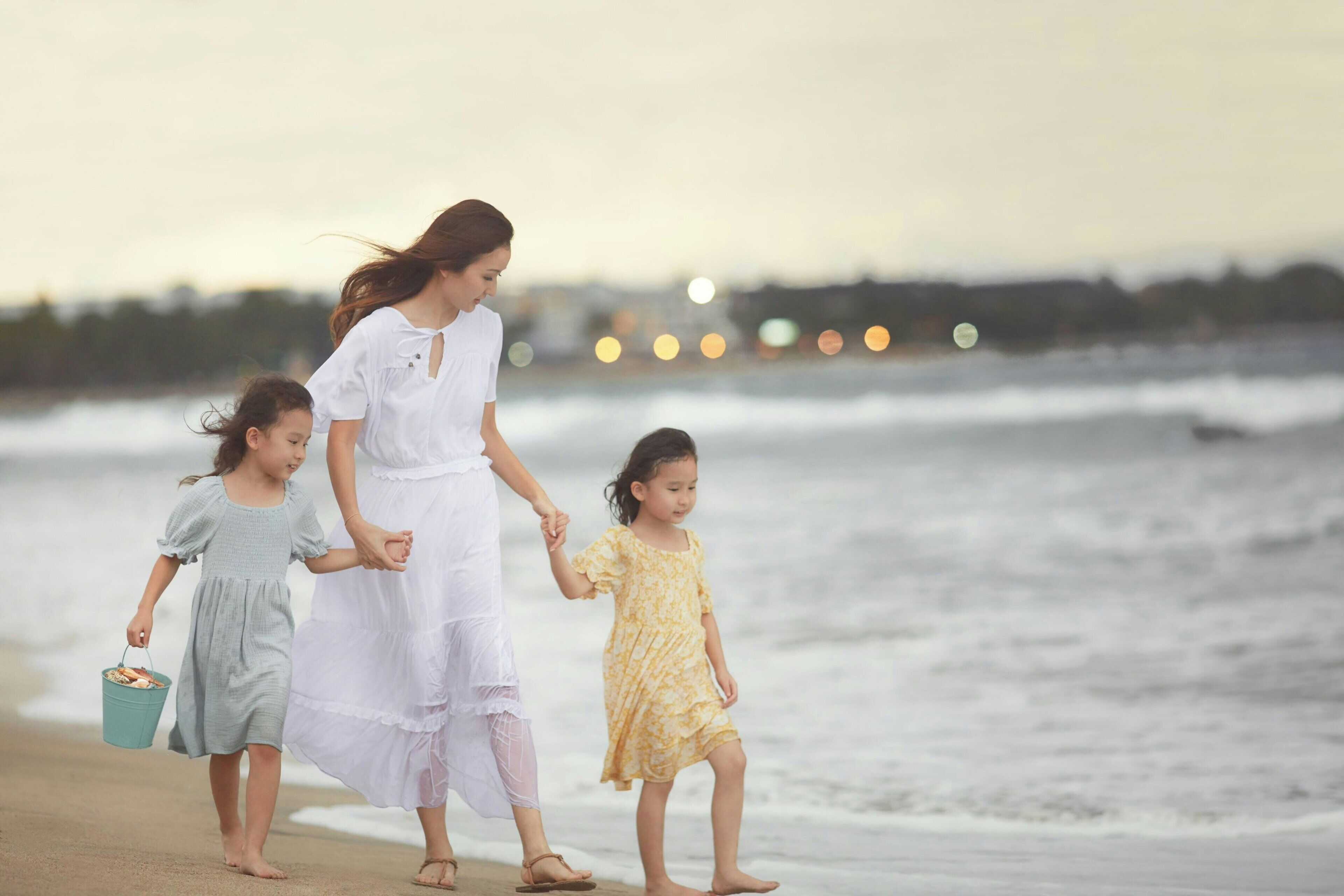 Escena de playa con una mujer y dos niños caminando por la orilla.