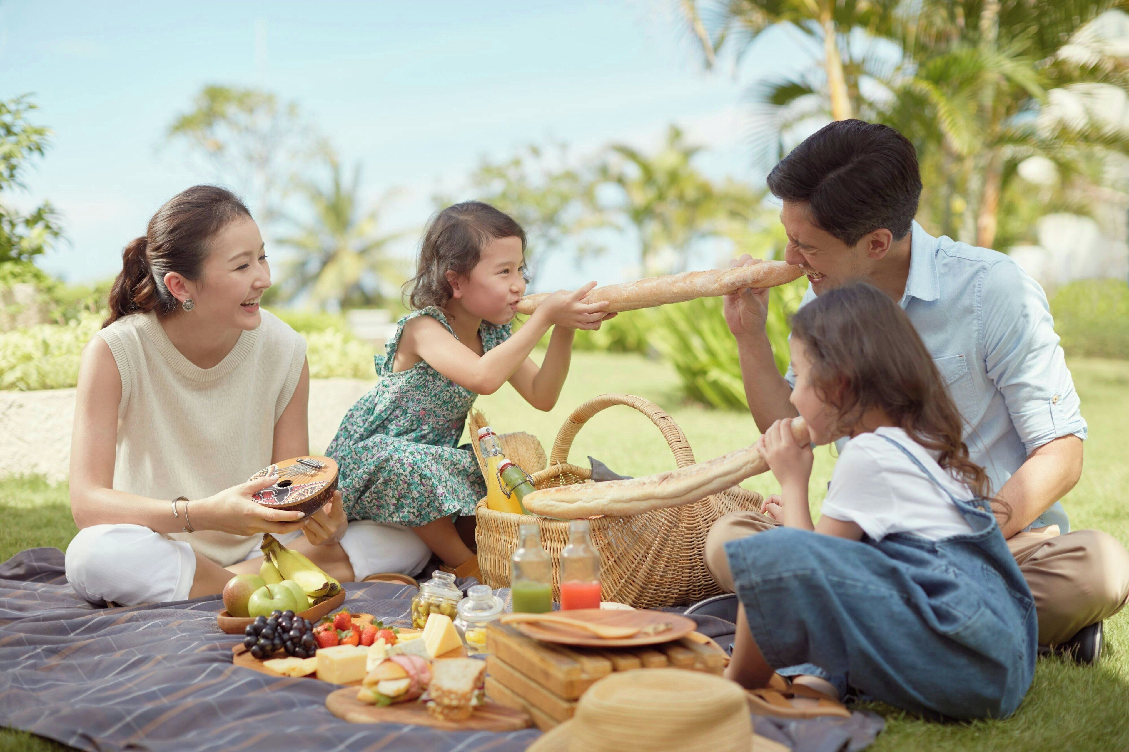 A family picnic with a blanket, food, and a basket in a park.