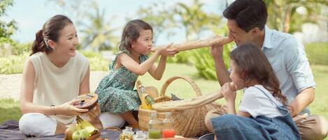 A family picnic with a blanket, food, and a basket in a park.