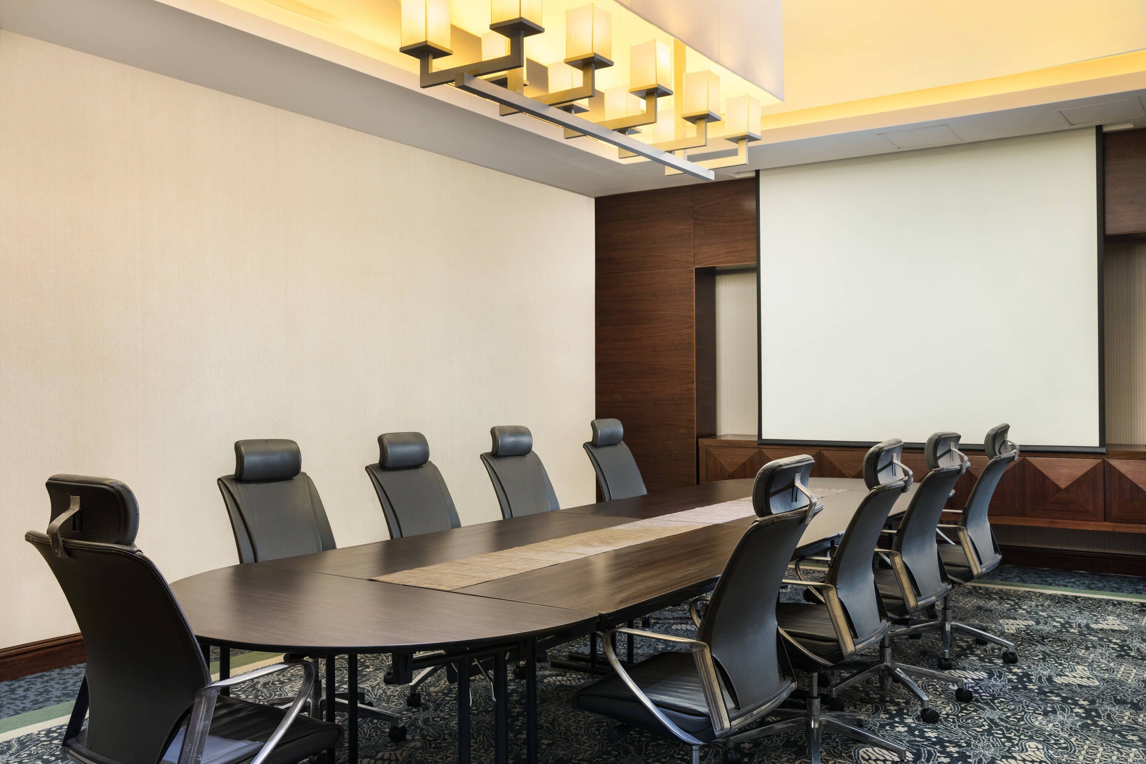A conference room with a long table, multiple chairs, and a projector screen.