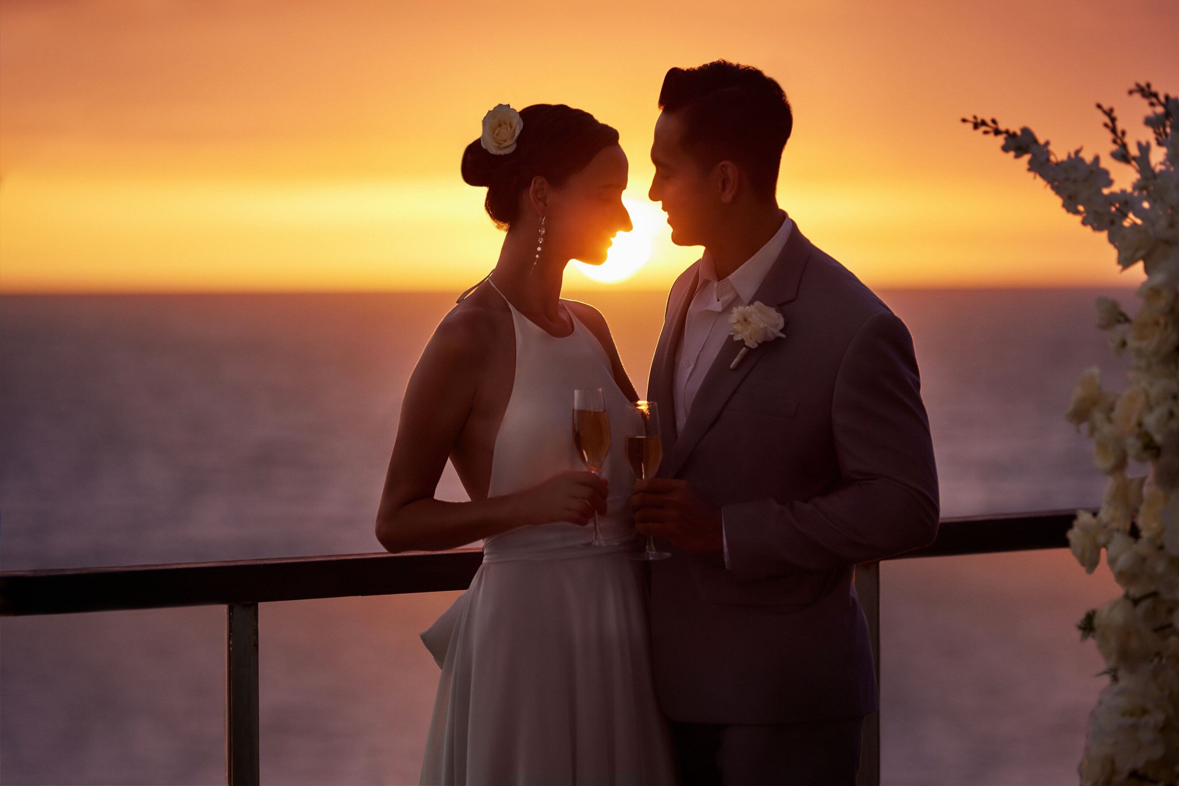 A couple holding champagne glasses against a sunset backdrop.
