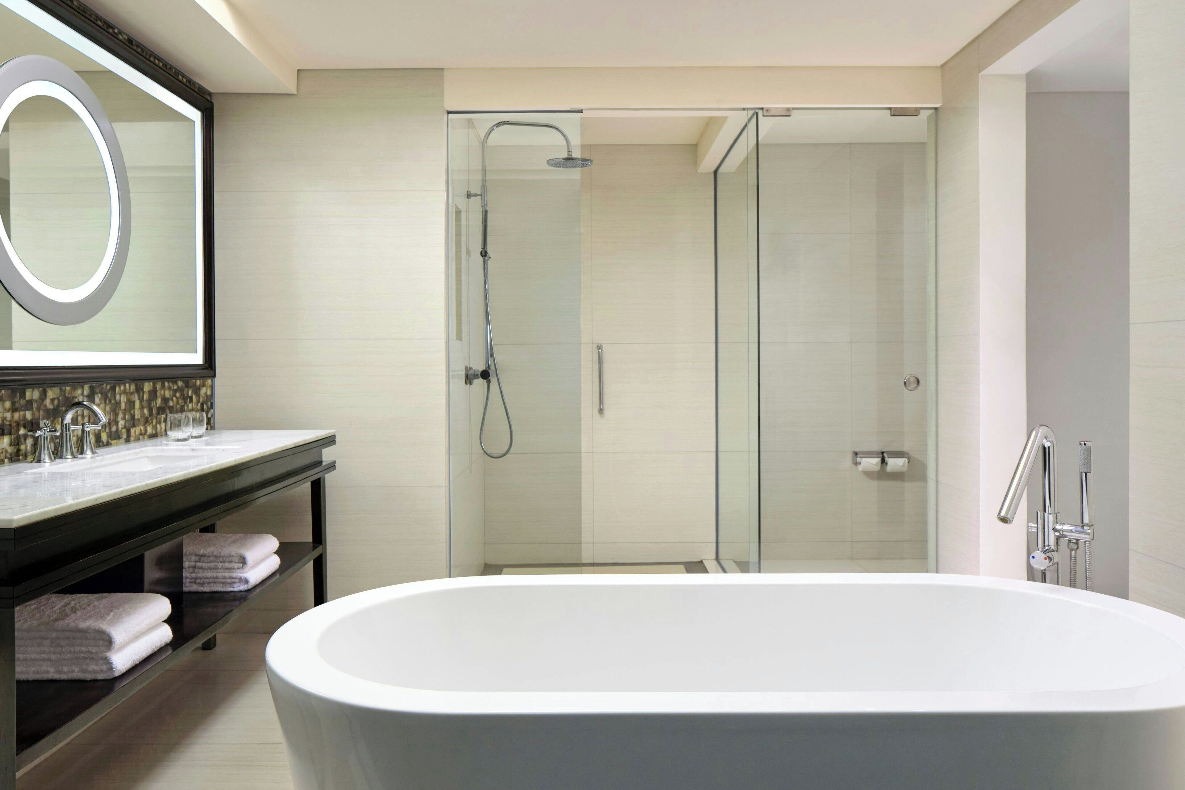 Ein modernes Badezimmer mit freistehender Badewanne, einer Duschkabine und einem Waschtisch mit Spiegel und Handtuchhalter.