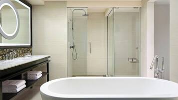 Un baño moderno con una bañera independiente, ducha con mampara de vidrio y tocador con espejo y toallero.