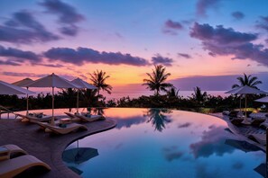 A poolside area with lounge chairs and umbrellas, palm trees, and a sunset view. - Sheraton Bali Kuta Resort (Kuta)