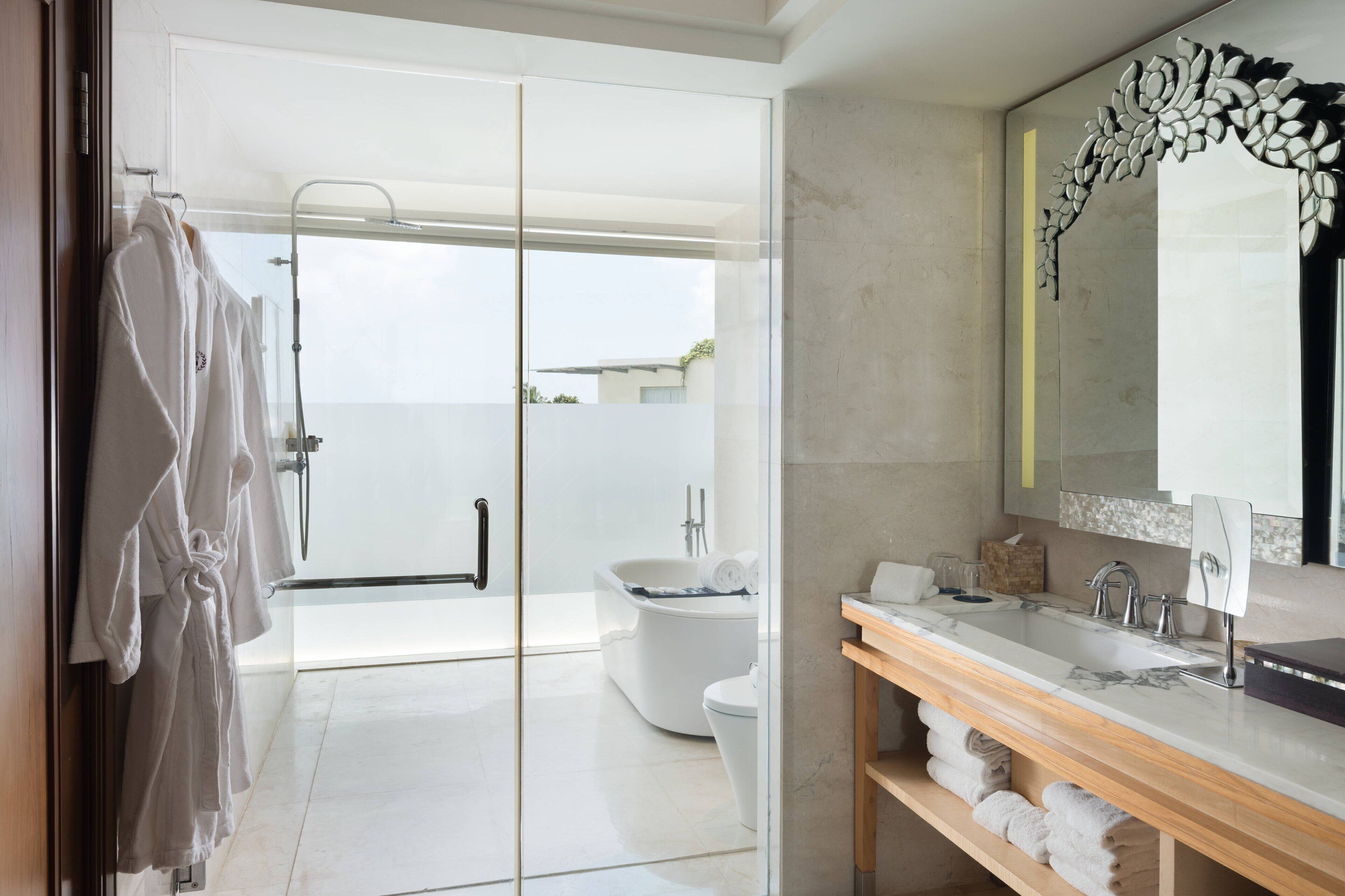 Un baño moderno con mampara de vidrio, bañera blanca y tocador de madera con un espejo grande.