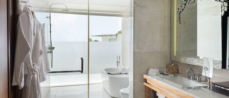 A modern bathroom with a glass shower door, a white bathtub, and a wooden vanity with a large mirror.