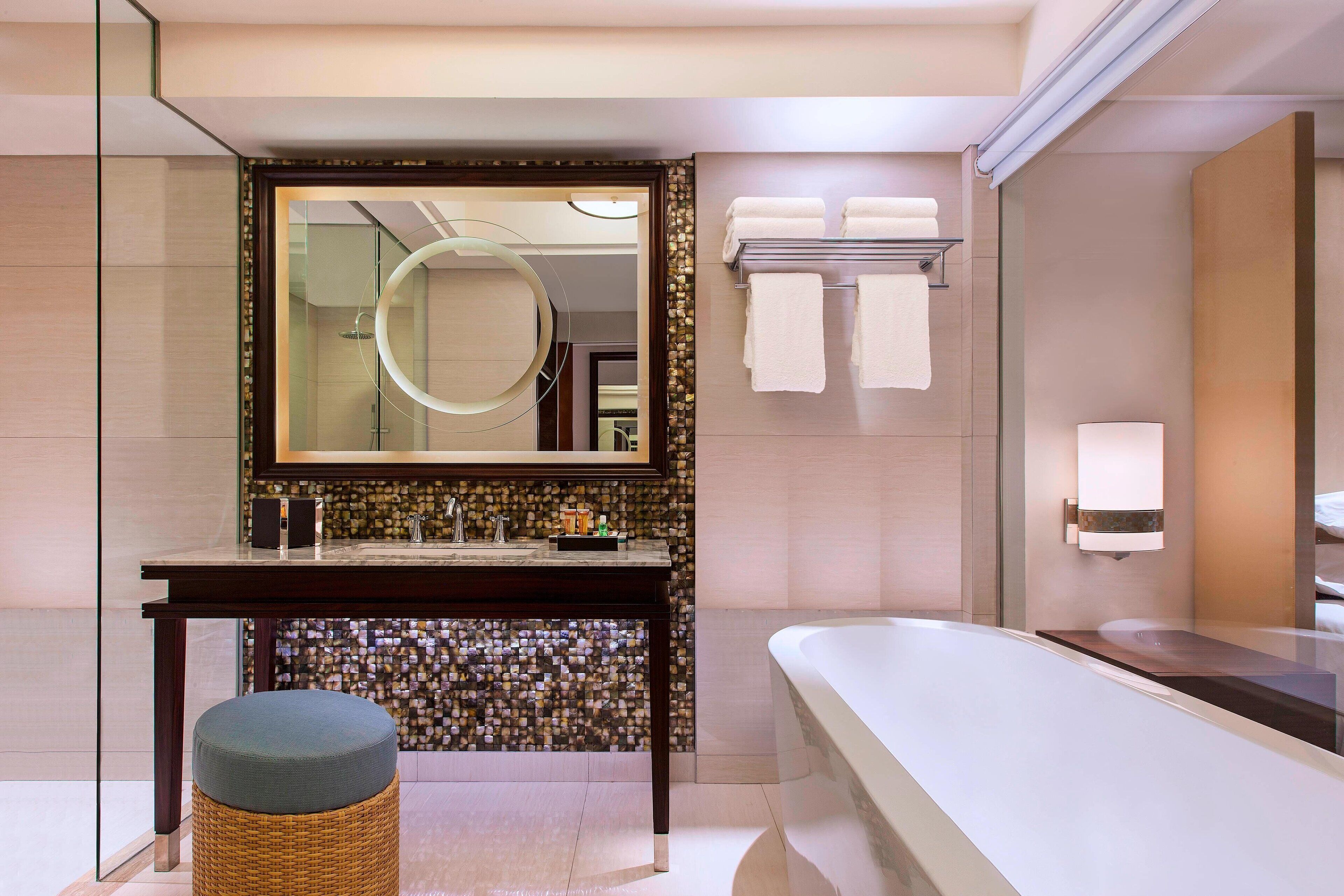 A modern bathroom with a large mirror, a bathtub, and a vanity with a mosaic backsplash.