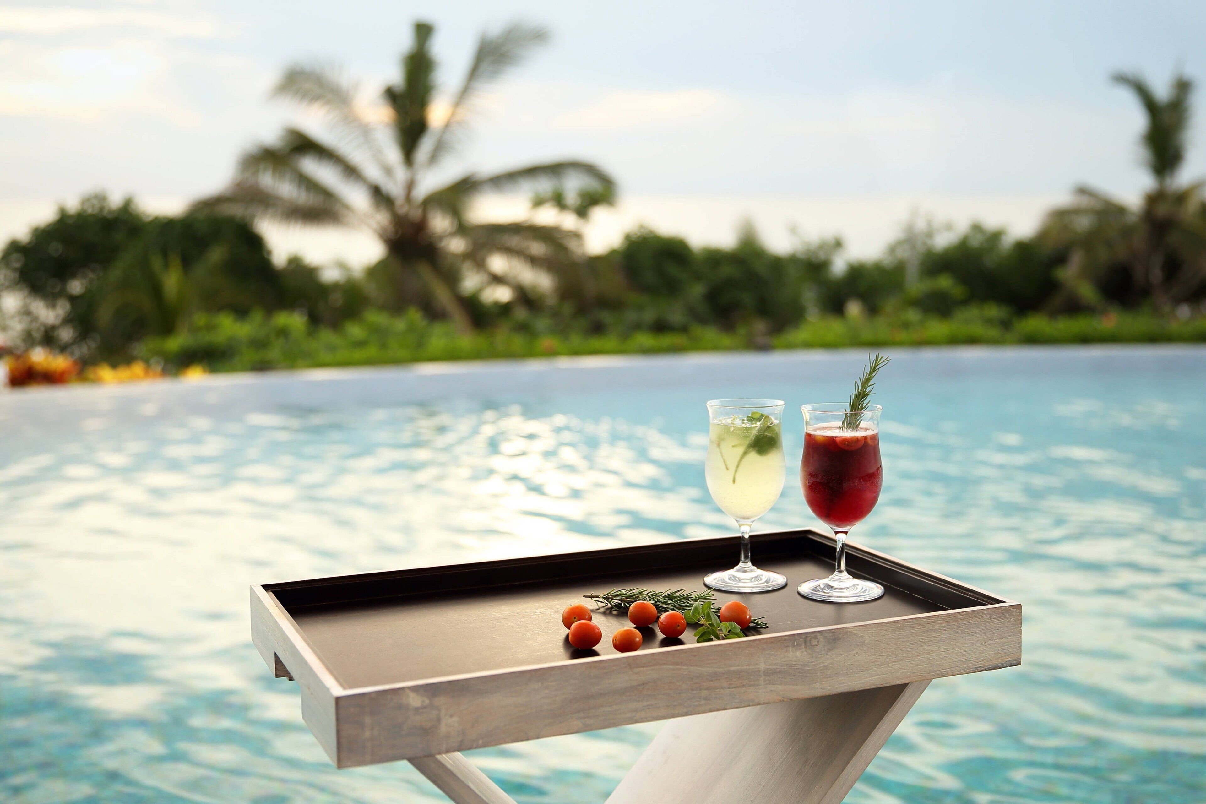 A tray with two drinks and some fruit by a poolside.