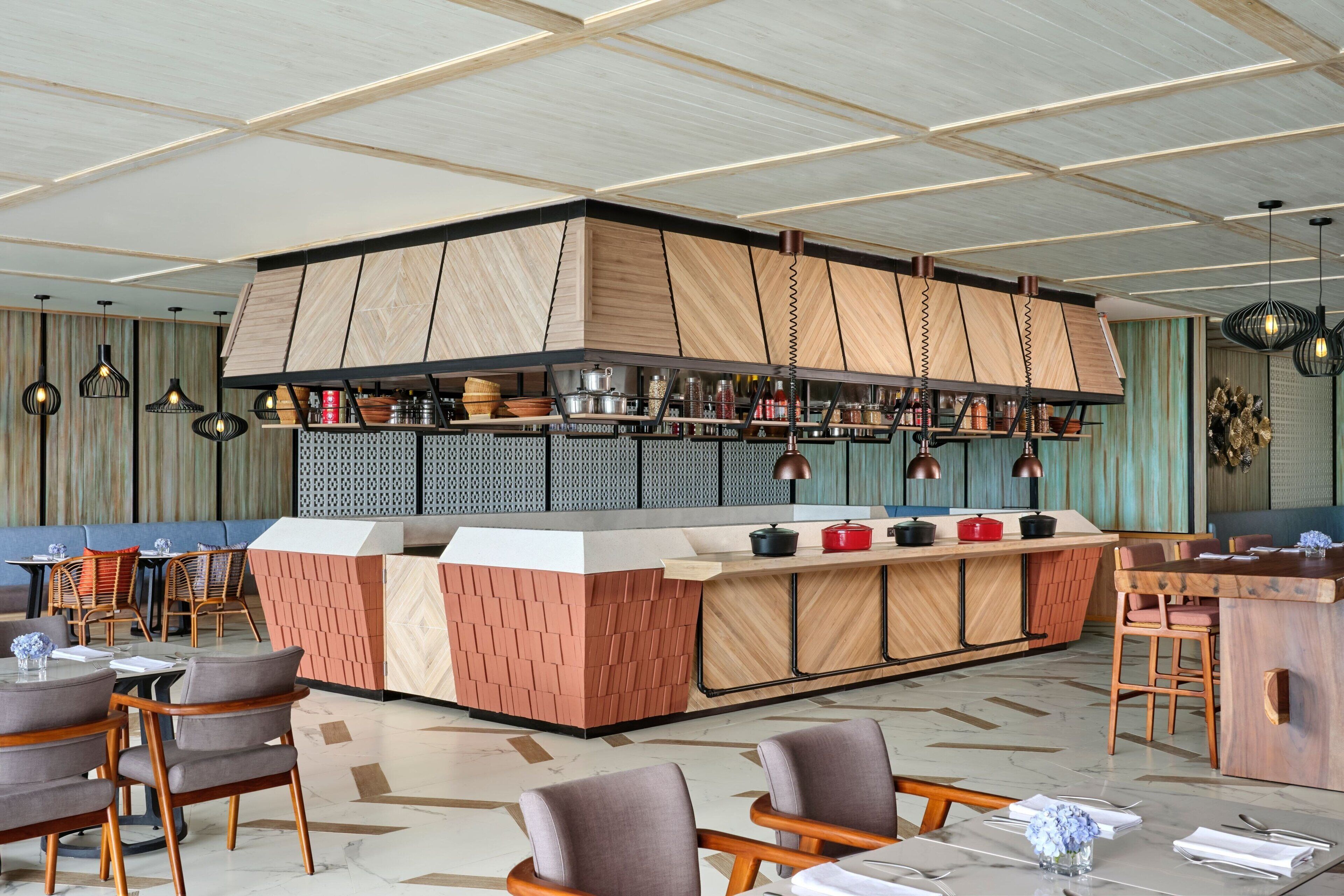 A modern restaurant with a central island, wooden panel walls, and a variety of seating options.
