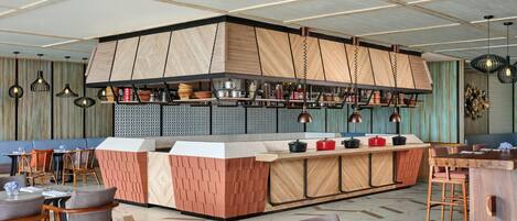 A modern restaurant with a central island, wooden panel walls, and a variety of seating options.