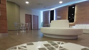 A modern interior with a white sofa, a glass-top table, and a dining area with chairs. - Idea Hotel Plus Savona (Savona)