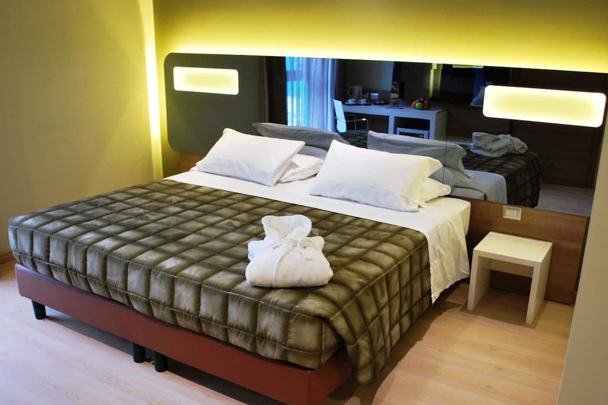 A neatly made bed with a quilted headboard, a bedside table, and a small stool.