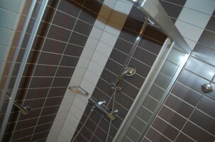 Un espacio de ducha con azulejos, puerta de cristal y ducha de acero cromado.