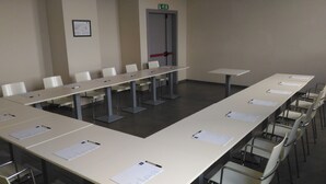 A conference room with long tables and chairs, a door with a red handle, and a framed sign on the wall. - Idea Hotel Plus Savona (Savona)