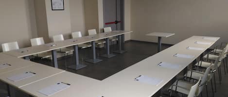 Un salón de conferencias con largas mesas y sillas, una puerta con picaporte rojo y un cartel enmarcado en la pared.