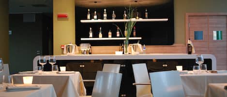 Un restaurante con mesas dispuestas para comer, una zona de bar con botellas y una planta decorativa.