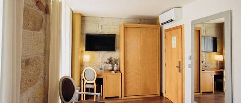 Habitación de hotel con pared de piedra, muebles de madera, televisor y espejo.