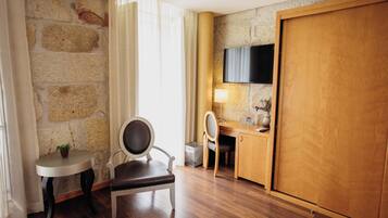 Een hotelkamer met een stenen muur, een houten bureau, een stoel, een aan de muur bevestigde televisie en een houten garderobe.