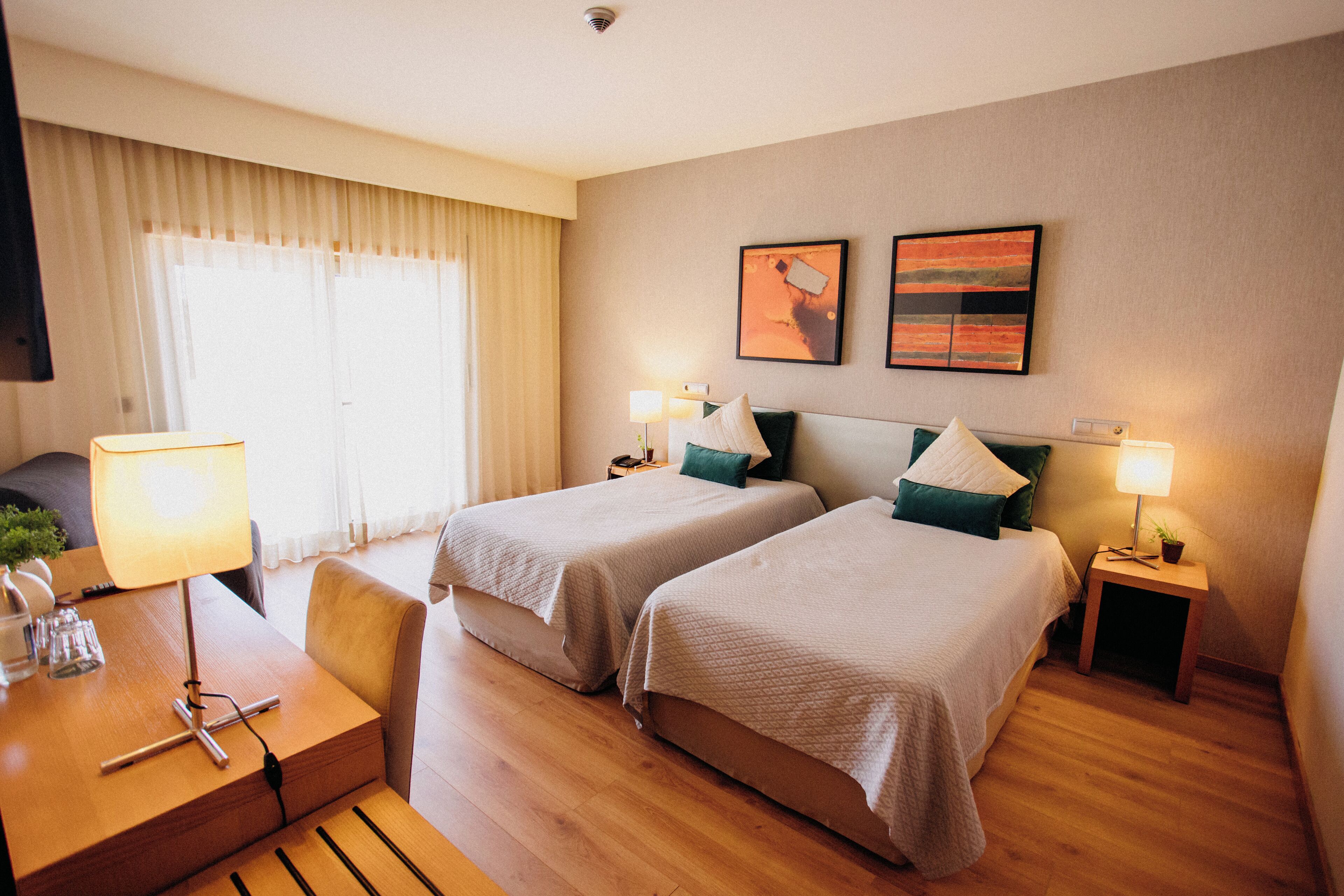 A hotel room with two beds, a desk with a lamp, a chair, and a small table with a plant.