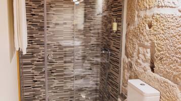 A bathroom with a glass-enclosed shower, a white toilet, and a stone wall.