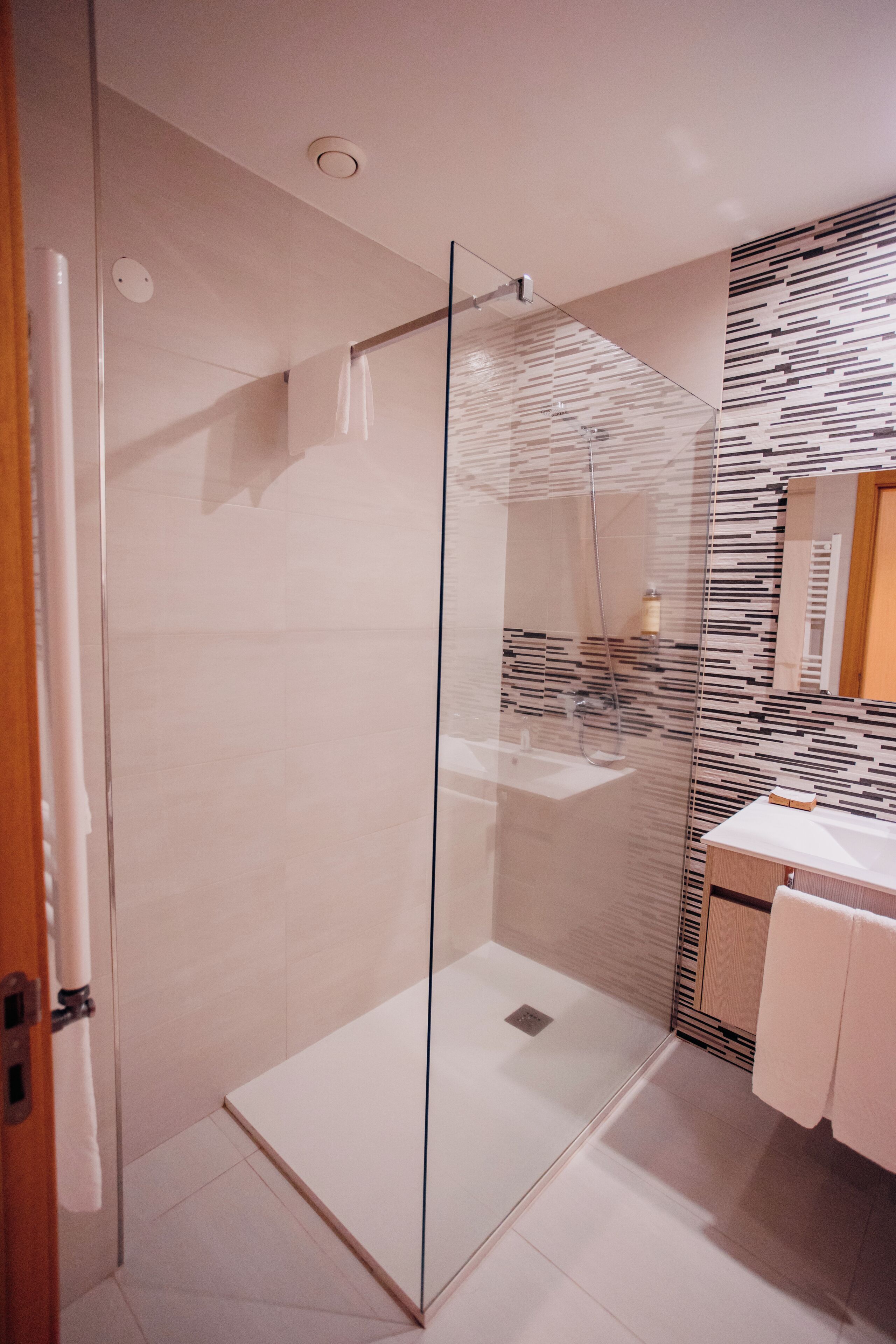 Une salle de bain moderne avec une douche à parois de verre, un meuble-lavabo en bois et un mur à motifs.