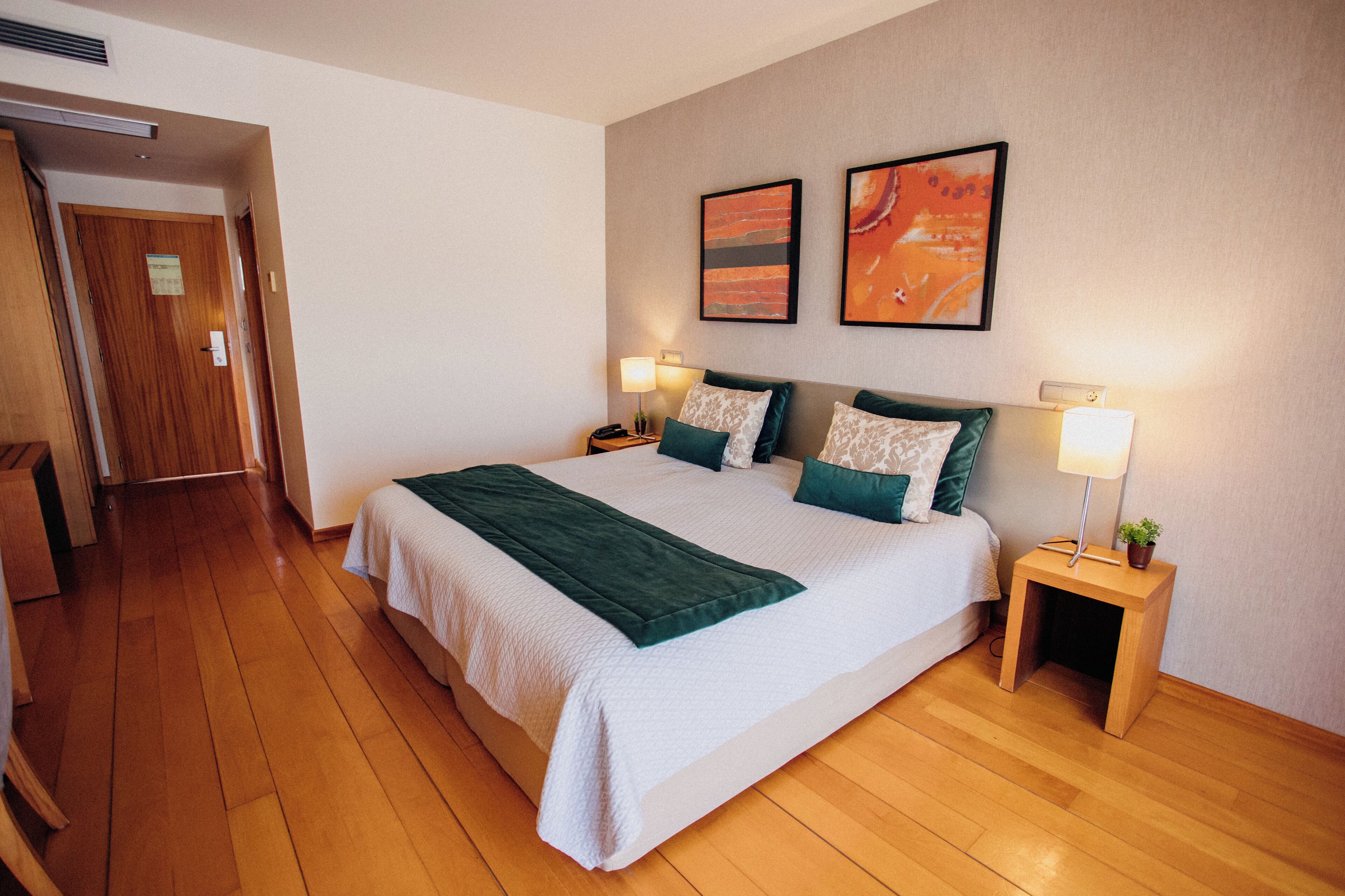 Un cuarto de hotel ordenado con una cama grande, dos mesitas de noche con lámparas, y dos cuadros enmarcados en la pared.