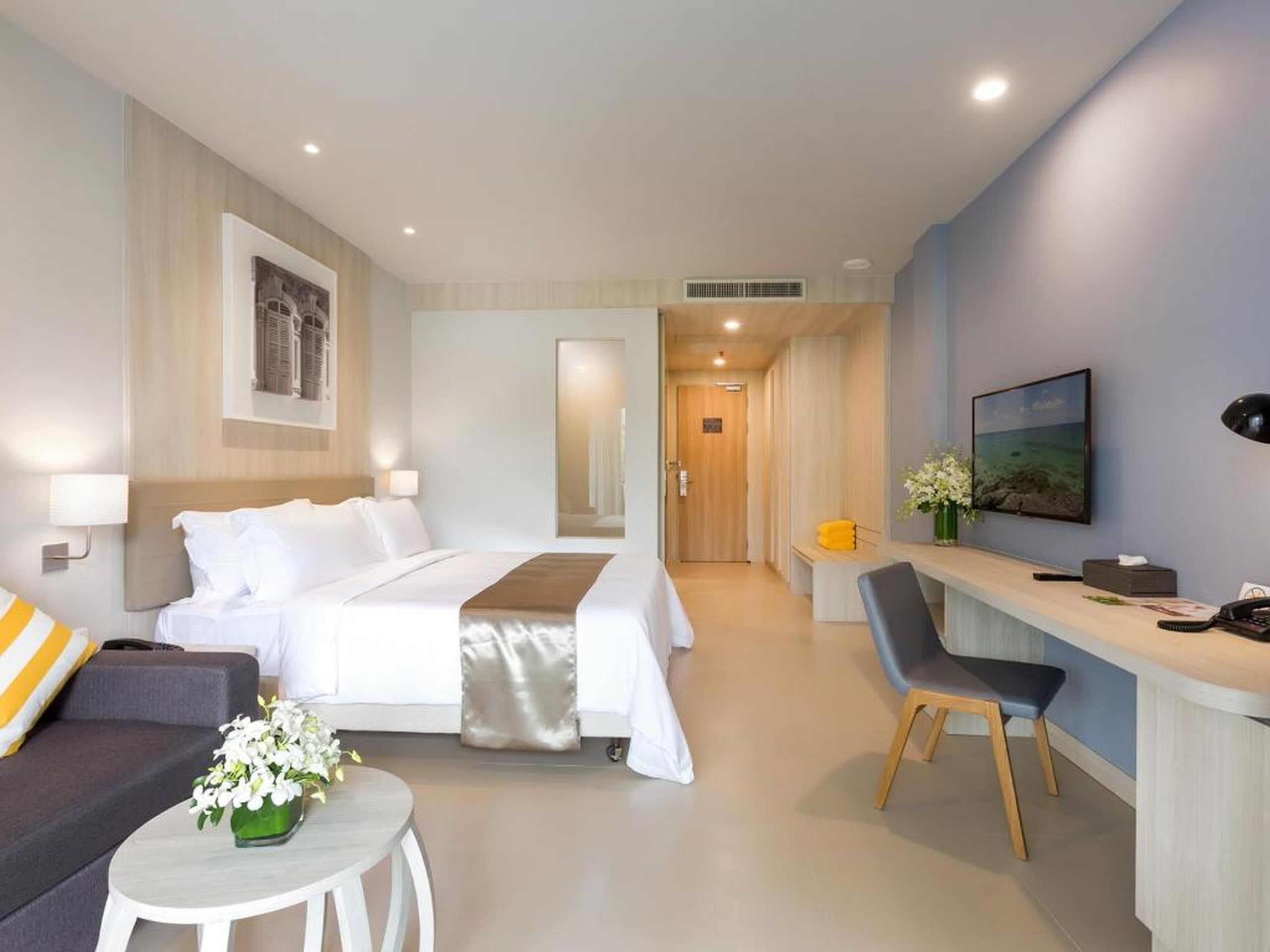 Une chambre d’hôtel avec un lit, un bureau, une chaise, un canapé et une petite table agrémentée de fleurs.