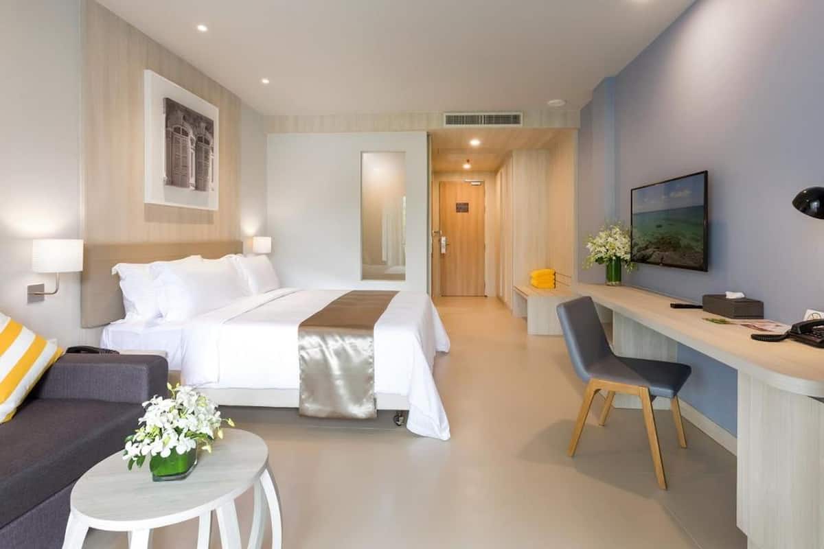 Une chambre d’hôtel avec un lit, un bureau, une chaise, un canapé et une petite table agrémentée de fleurs.