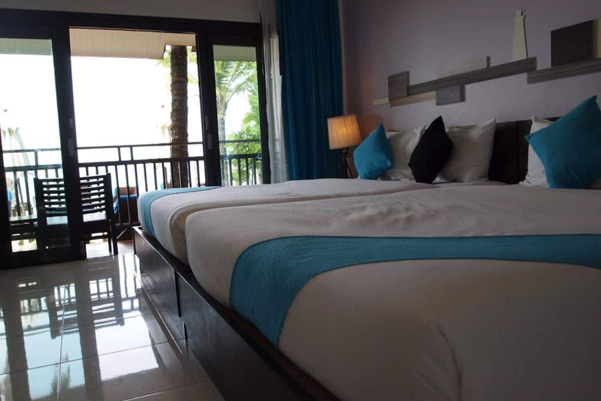 A hotel room with a large bed, a balcony with a view, and a door leading outside.