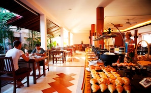 Een restaurant met houten tafels en stoelen, een buffet met gebak, en uitzicht op het omliggende landschap.