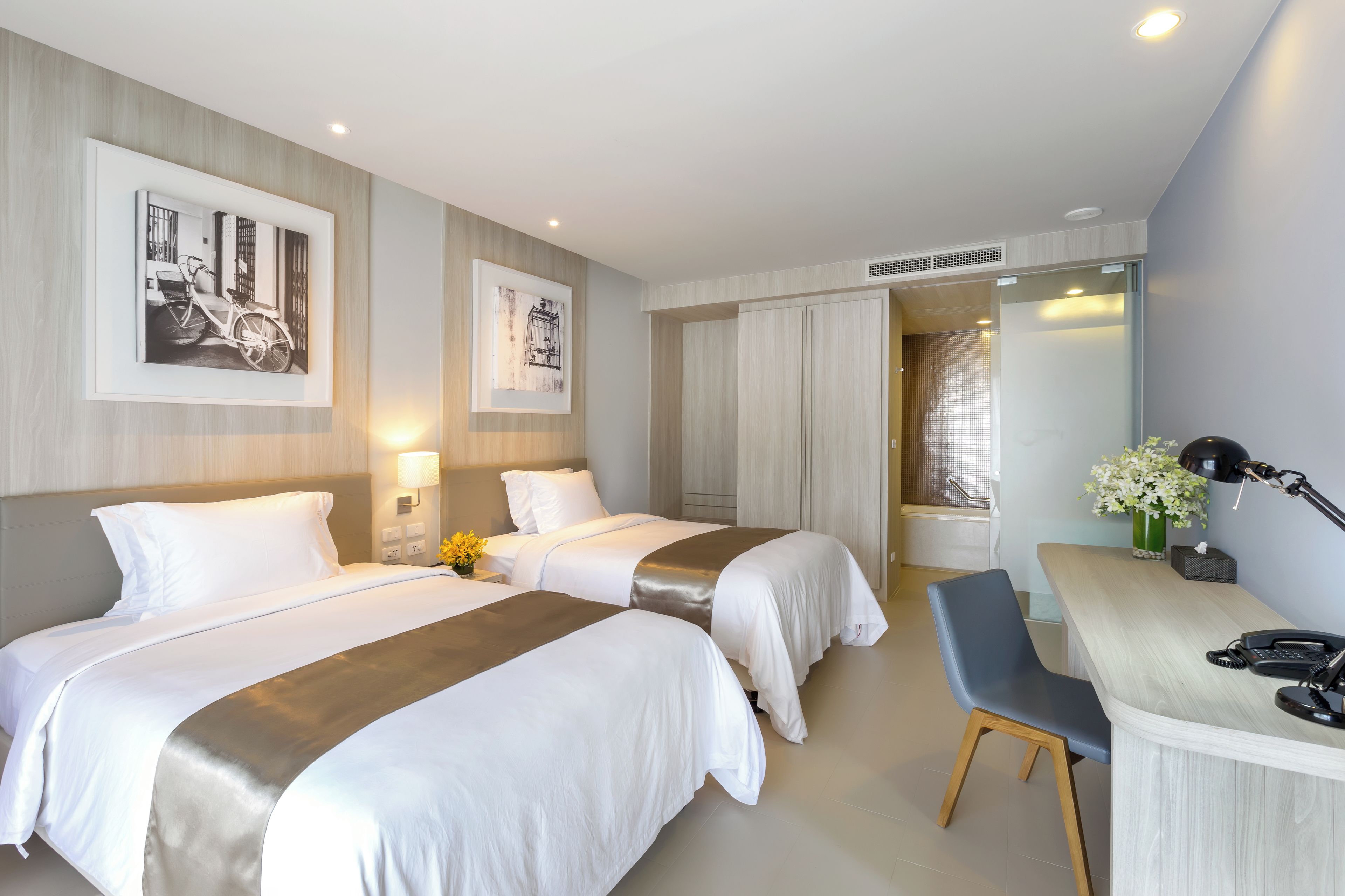 A hotel room with two beds, a desk, a chair, a phone, and a lamp.