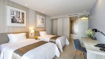 A hotel room with two beds, a desk, a chair, a phone, and a lamp.
