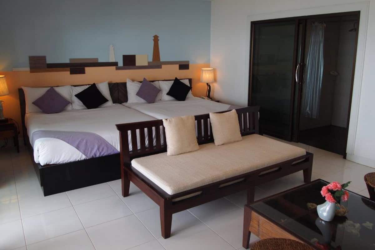 A hotel room with two beds, a sofa, a glass table, and a view of the outdoors.