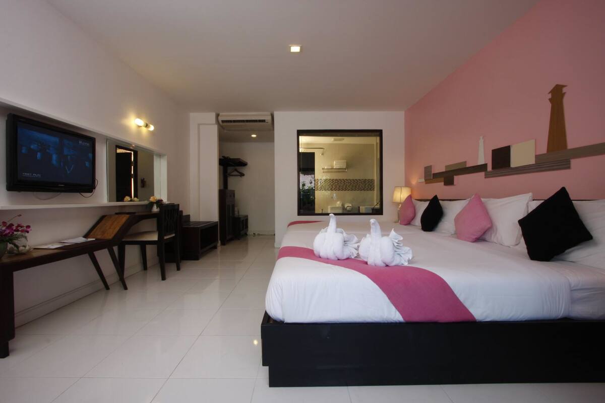 A hotel room with a large bed, a desk with a chair, a television, and a bathroom visible through an open door.