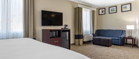 Habitación de hotel con una cama grande, televisión de pantalla plana, kitchenette pequeño, sofá y piso alfombrado.