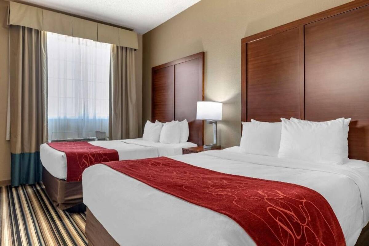A hotel room with two beds, a large wooden headboard, a window with curtains, and a striped carpet.