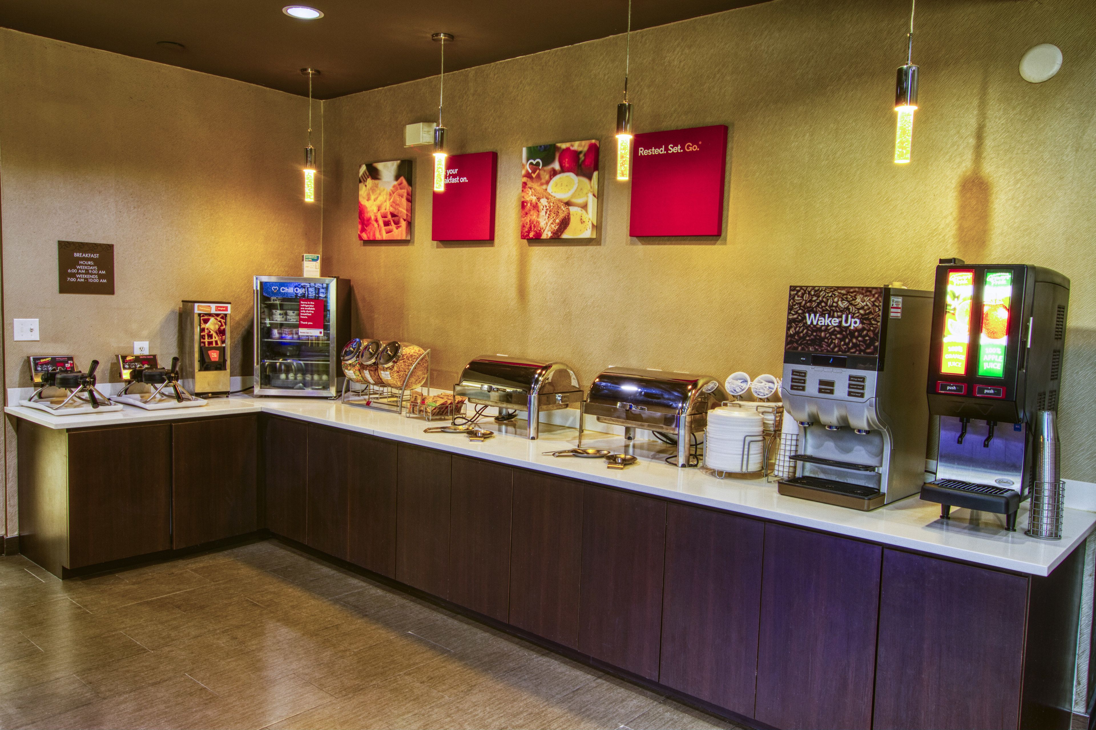 Un mostrador de buffet con distintas estaciones de comida, una máquina de café y un dispensador de zumo.
