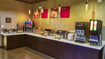 Un mostrador de buffet con distintas estaciones de comida, una máquina de café y un dispensador de zumo.