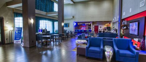 A spacious lobby with a bar area, seating, and a television screen.