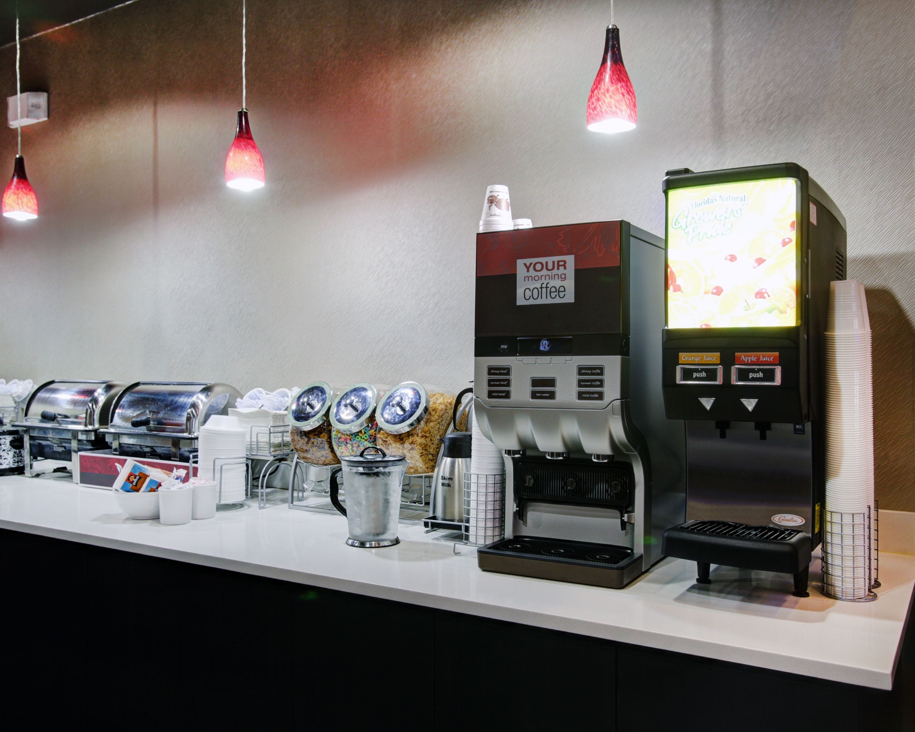 A coffee station with multiple coffee machines, dispensers, and a menu display.
