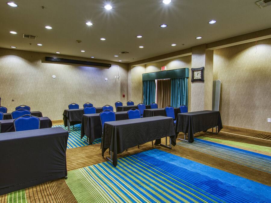Un salón de conferencias con filas de mesas y sillas, un reloj en la pared y piso alfombrado.