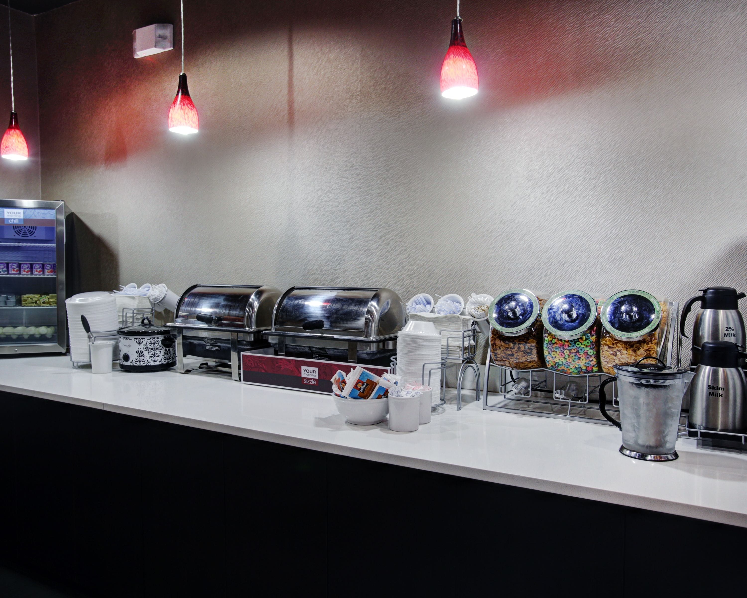 A breakfast bar with coffee machines, milk dispensers, and cereal containers.